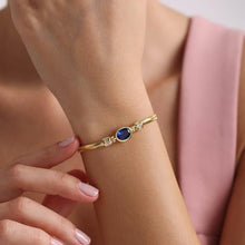 Gold bracelet with a blue gemstone on a wrist against a pink background