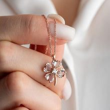 Rose gold necklace with a clover-shaped pendant held by a hand against a neutral background