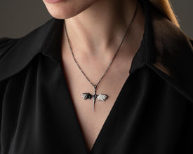 Person wearing a black shirt with a unique necklace featuring a butterfly pendant.