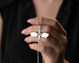 Hand holding a silver dragon necklace against a dark background