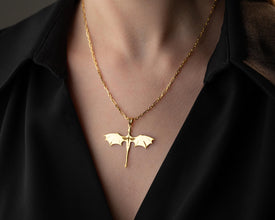 Gold bat-shaped pendant necklace on a person wearing a black shirt.