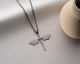 Silver bat pendant necklace on a light surface with a beige vase.