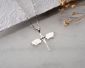 Silver dragon pendant necklace on a light gray surface with dried flowers.