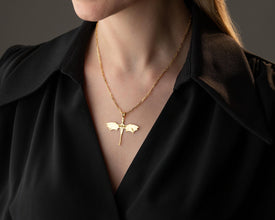 Gold necklace with a bat pendant worn by a person against a dark background