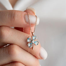 Rose gold necklace with a clover-shaped pendant held by a hand against a neutral background