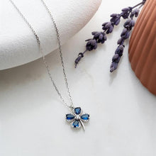 Silver necklace with a blue pendant on a white surface with lavender flowers.