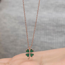 Green four-leaf clover necklace on a chain against a gray background