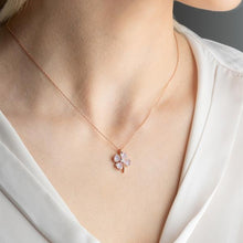 Necklace with a floral pendant worn by a person in a white shirt.