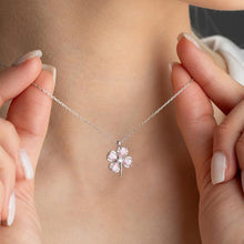 Silver necklace with a clover-shaped pendant held by hands against a neutral background