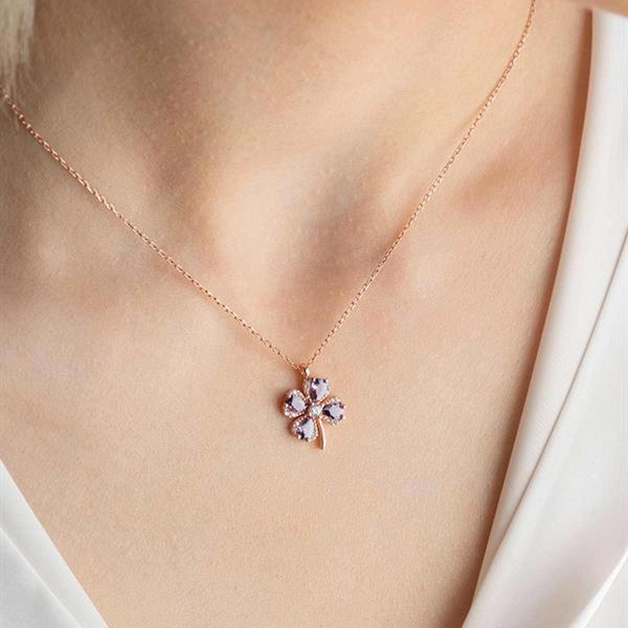 Rose gold necklace with a floral pendant on a person wearing a white top.