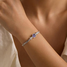 Silver bracelet with a purple gemstone on a wrist against a neutral background