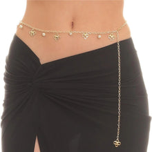 Gold chain belt with floral designs worn by a person on a black skirt against a white background