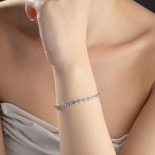 Close-up of a person's arm wearing a delicate bracelet with blue stones on a neutral background