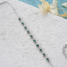 Silver bracelet with green gemstones on a textured surface with flowers in the background