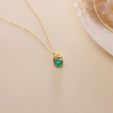 Gold necklace with a green pendant on a beige background