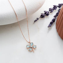 Rose gold necklace with a clover-shaped pendant on a white surface with lavender.