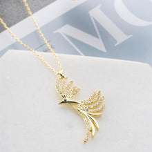 Gold necklace with a leaf-like pendant on a light gray surface