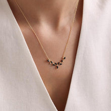Gold necklace with black stones worn by a person in a white outfit