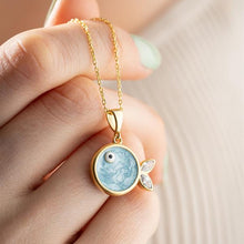 Gold necklace with a blue pendant held by a hand against a neutral background