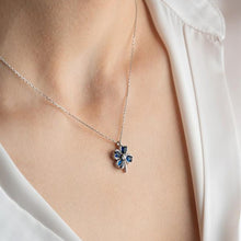 Necklace with a floral pendant featuring blue stones worn by a person in a white shirt.