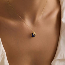 Gold necklace with a blue pendant on a person wearing a white shirt.