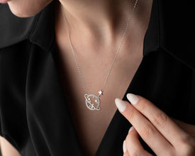 A cosmic-inspired Saturn pendant necklace laid on a dark galaxy background, enhancing its celestial beauty.