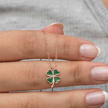 Green four-leaf clover necklace on a hand against a neutral background