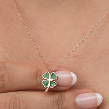 Gold necklace with a green four-leaf clover pendant held by a hand.