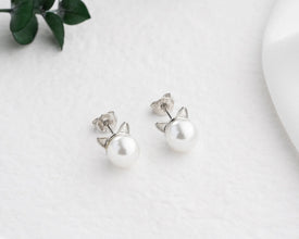Pearl cat-shaped earrings on a light background