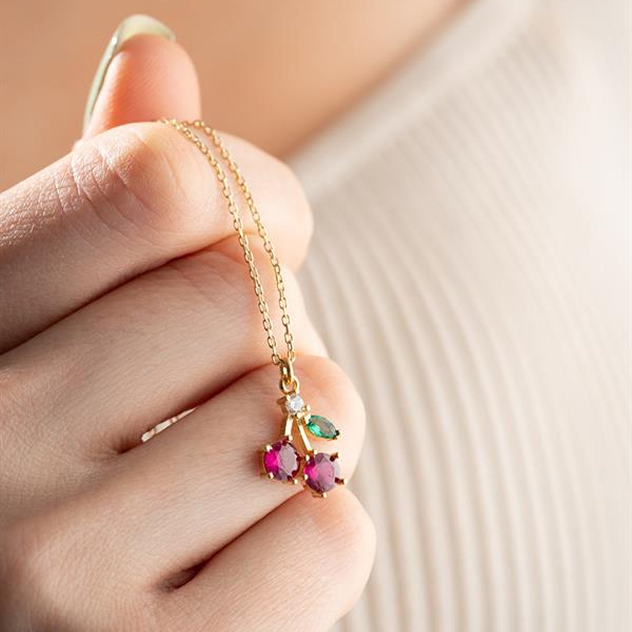 Gold necklace with colorful gemstones held by a hand against a neutral background