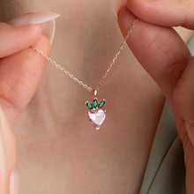 Necklace with a heart-shaped pendant featuring pink gemstone and green accents, held by hands.
