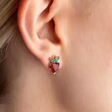 Close-up of an ear wearing a strawberry-shaped earring with green leaves.