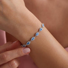 Silver bracelet with blue stones on a wrist against a pink background