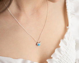 A sterling silver bird charm necklace with a radiant opal gemstone, symbolizing wisdom and freedom.