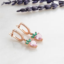 Rose gold earrings with pink and green gemstones on a white background with lavender.