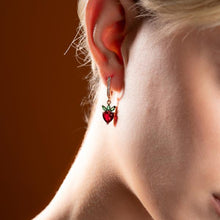 Close-up of a person wearing a strawberry-shaped earring with a red background