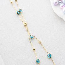 Gold necklace with blue evil eye charms on a light gray background