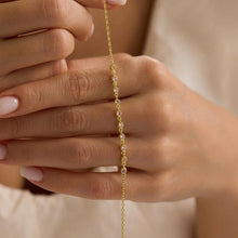 Close-up of a hand holding a delicate gold bracelet with small stones.