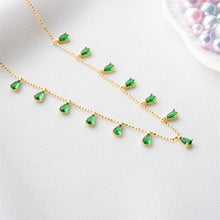 Gold necklace with green gemstones on a light gray background