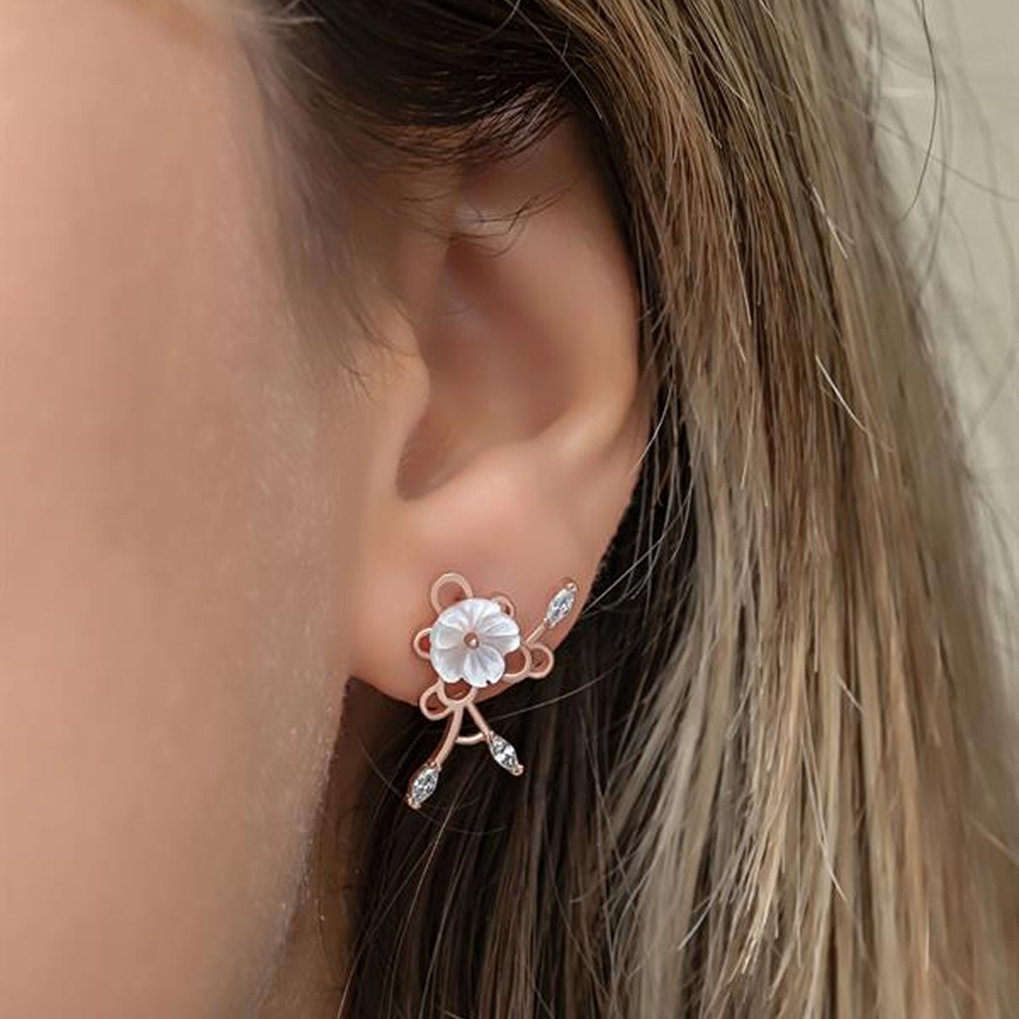 Close-up of an ear wearing a delicate floral earring with rose gold and clear gemstones.
