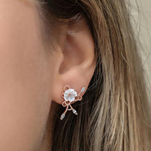 Close-up of an ear wearing a delicate floral earring with rose gold and clear gemstones.