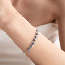 Close-up of a person's arm wearing a bracelet with blue stones on a neutral background