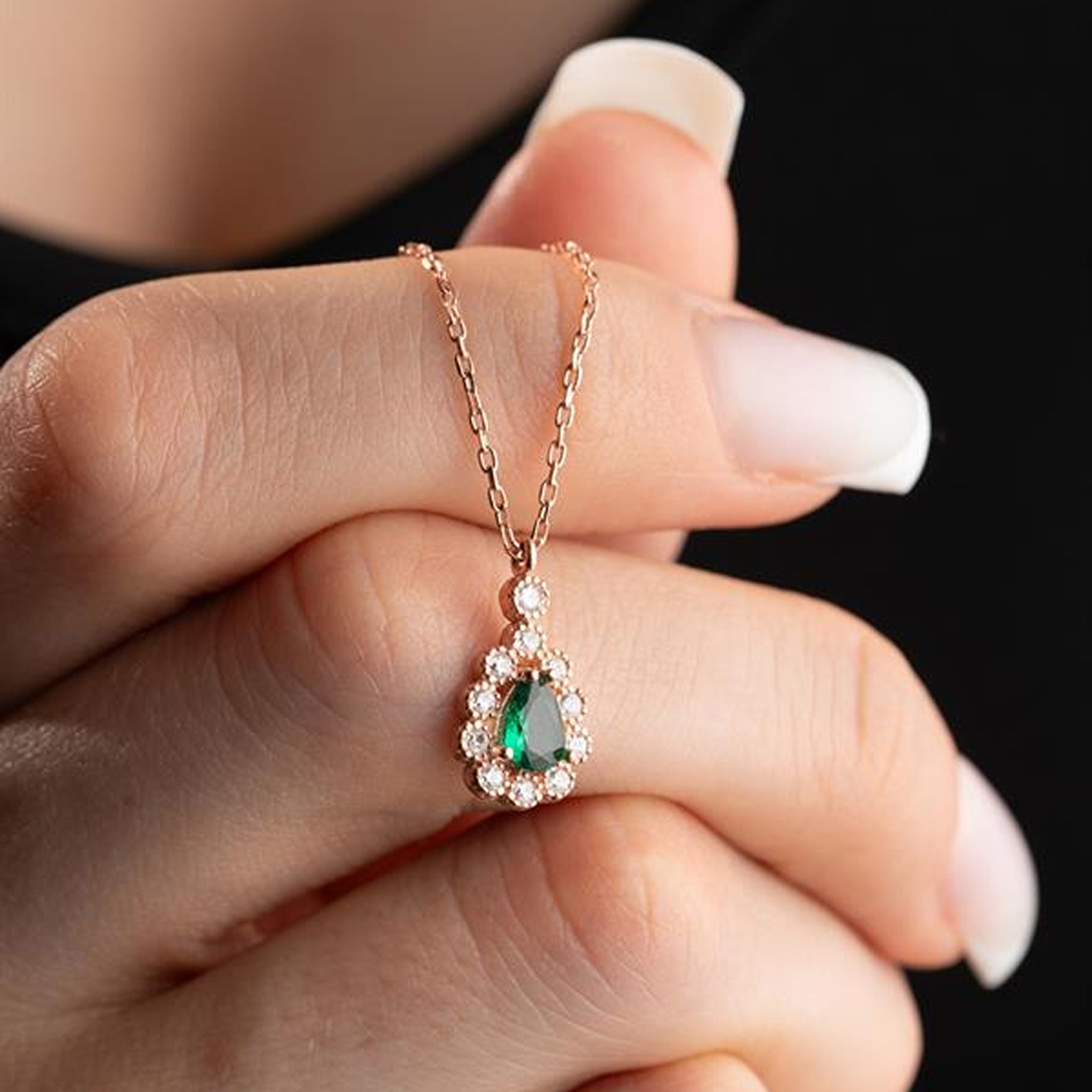 Rose gold necklace with a green gemstone held by a hand against a black background