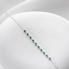 Silver bracelet with green gemstones on a white cushion