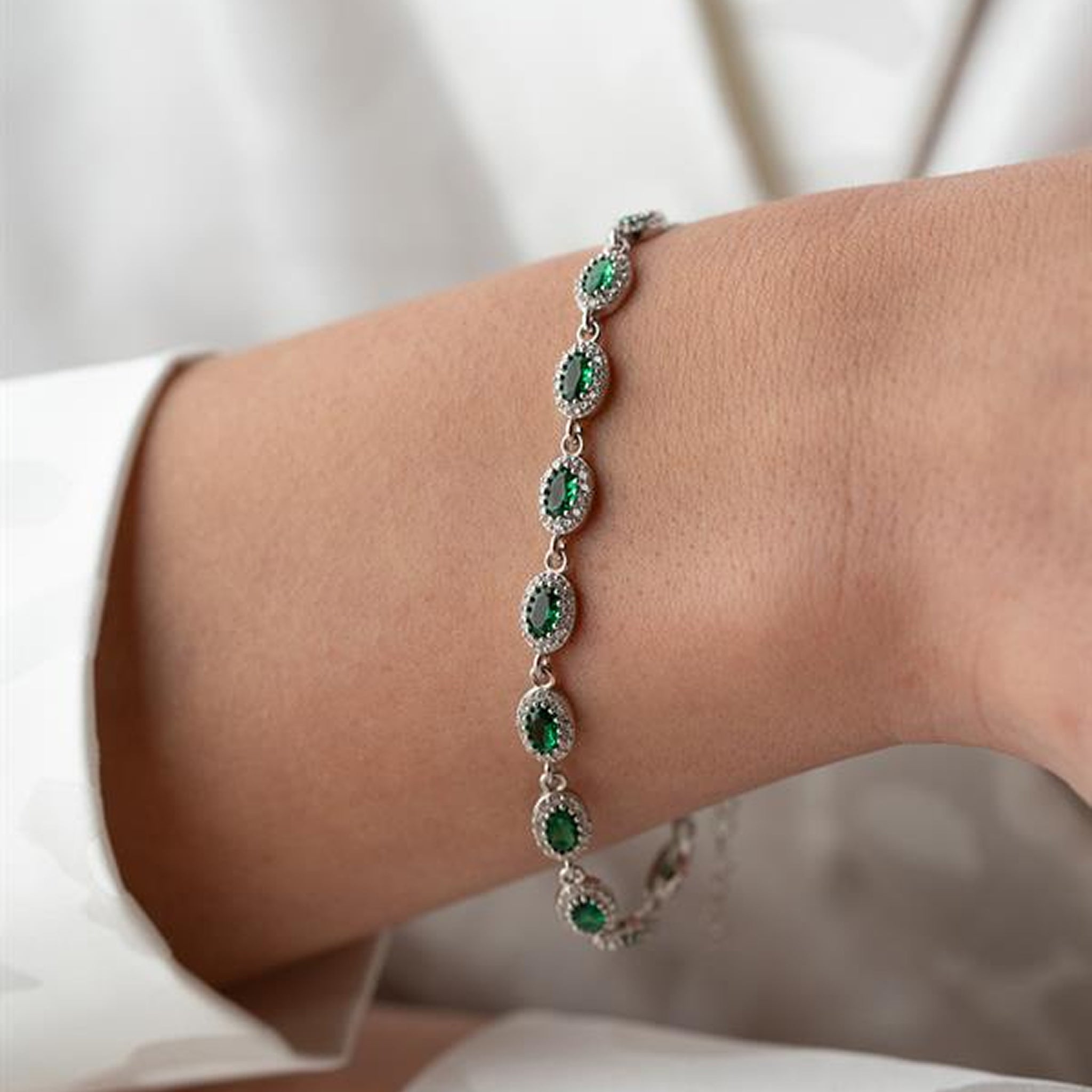 Silver bracelet with green gemstones on a wrist against a neutral background