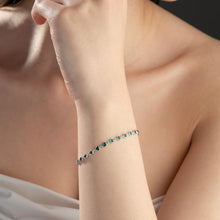 Close-up of a person's wrist wearing a delicate bracelet with small green stones.