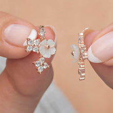 Rose gold floral earrings held between fingers against a neutral background