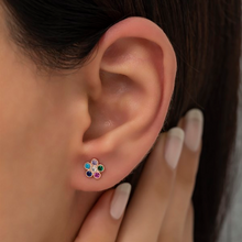 Close-up of an ear wearing a colorful flower-shaped earring with a hand touching the earlobe.