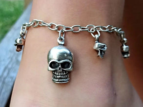 Silver skull charm bracelet on a wrist with a blurred background