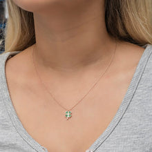 Close-up of a necklace with a clover pendant on a person wearing a gray top.